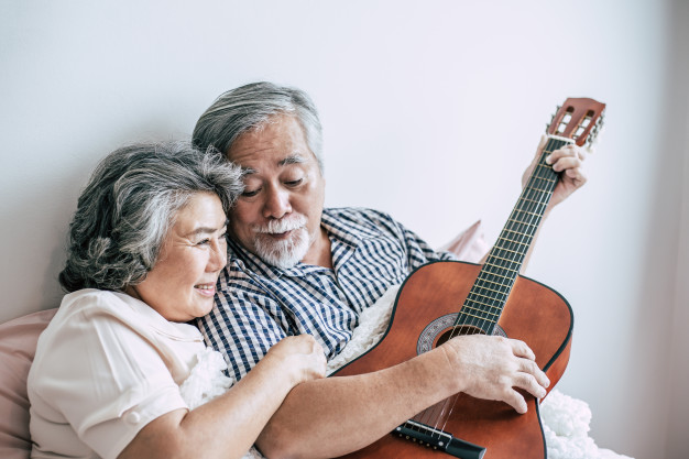 senior couple relax playing acoustic guitar bed room